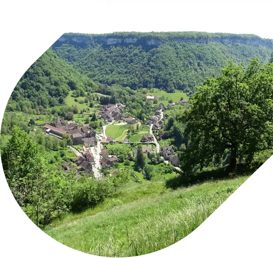 C'est un paysage du village durant le printemps. Au premier plan, il y a un arbre et des arbustres. Au second plan il y a le village avec deux artères principales. A gauche on peut voir l'Abbaye. A droite des maisons aux toits rouges et bruns. Au dernier plan, on peut voir la reculée.